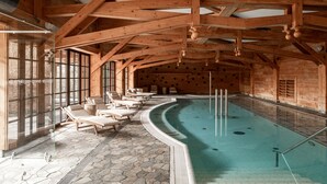 An indoor swimming pool with stone flooring, wooden beams, and lounge chairs. - ARIES Hotel & SPA (Zakopane)