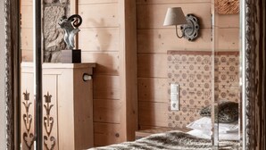 A wooden cabin room with a bed, a nightstand, a lamp, and a stone wall. - ARIES Hotel & SPA (Zakopane)