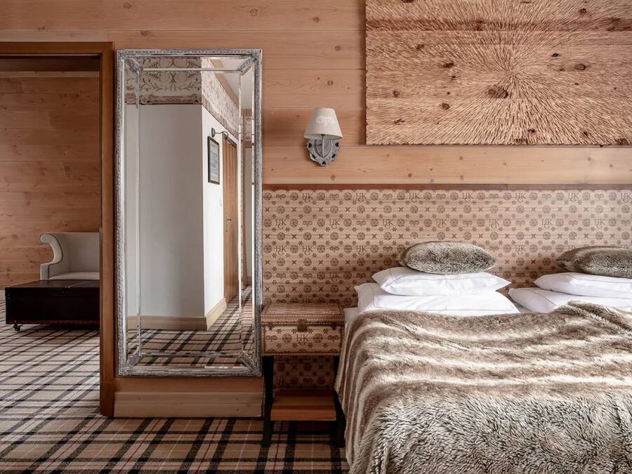 A bedroom with a large mirror, a bed with a fluffy blanket, a bedside table with a lamp, and a patterned wall.