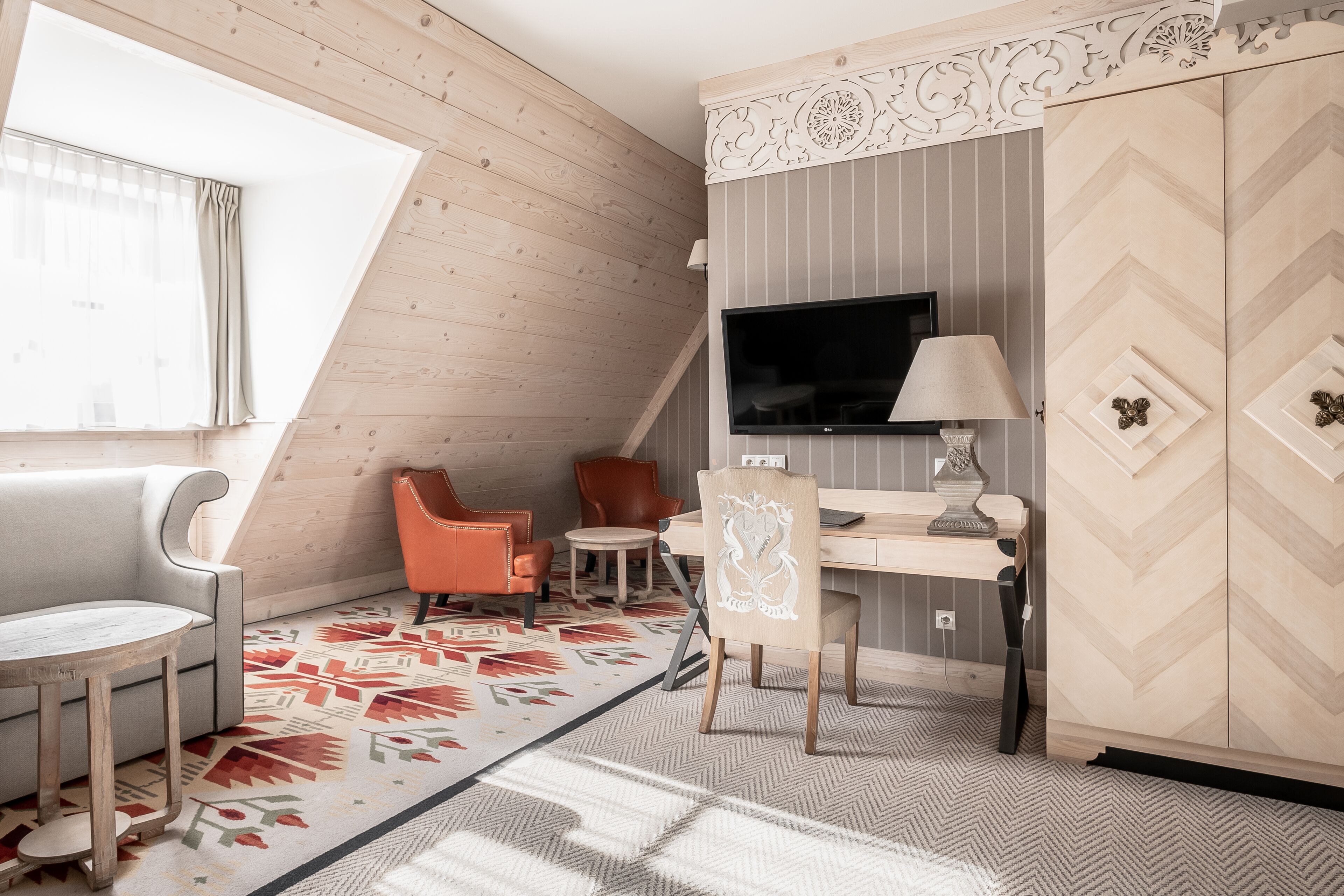 A cozy room with a sloped ceiling, a desk with a TV, a sofa, and two chairs.