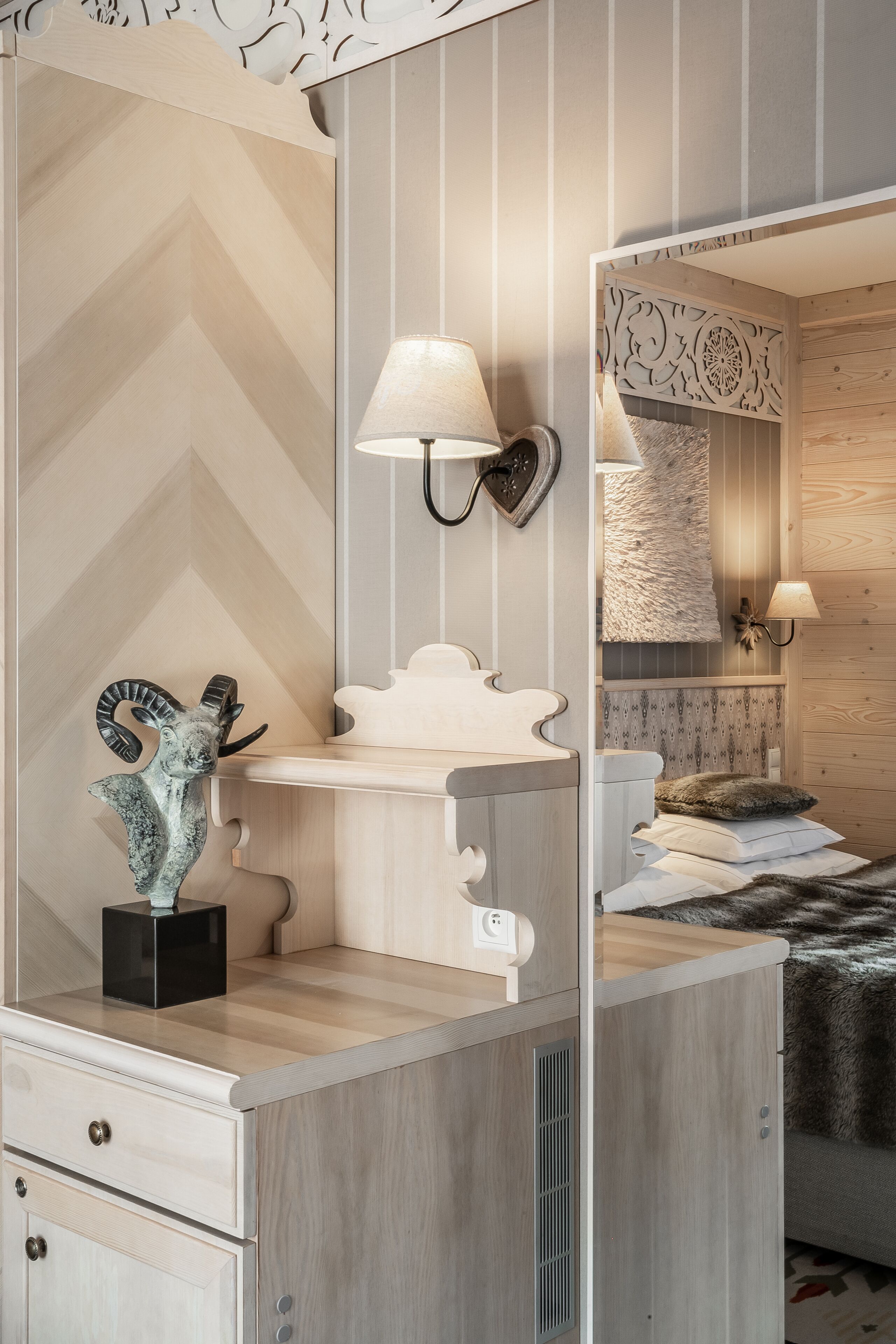 A bedroom with a wooden headboard, a bedside lamp, a decorative sculpture, and a fluffy throw blanket.