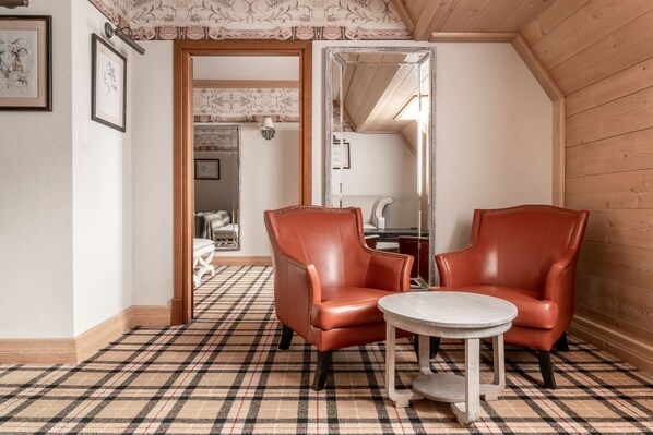 A room with a plaid carpet, two leather chairs, a small round table, and a mirror on the wall.