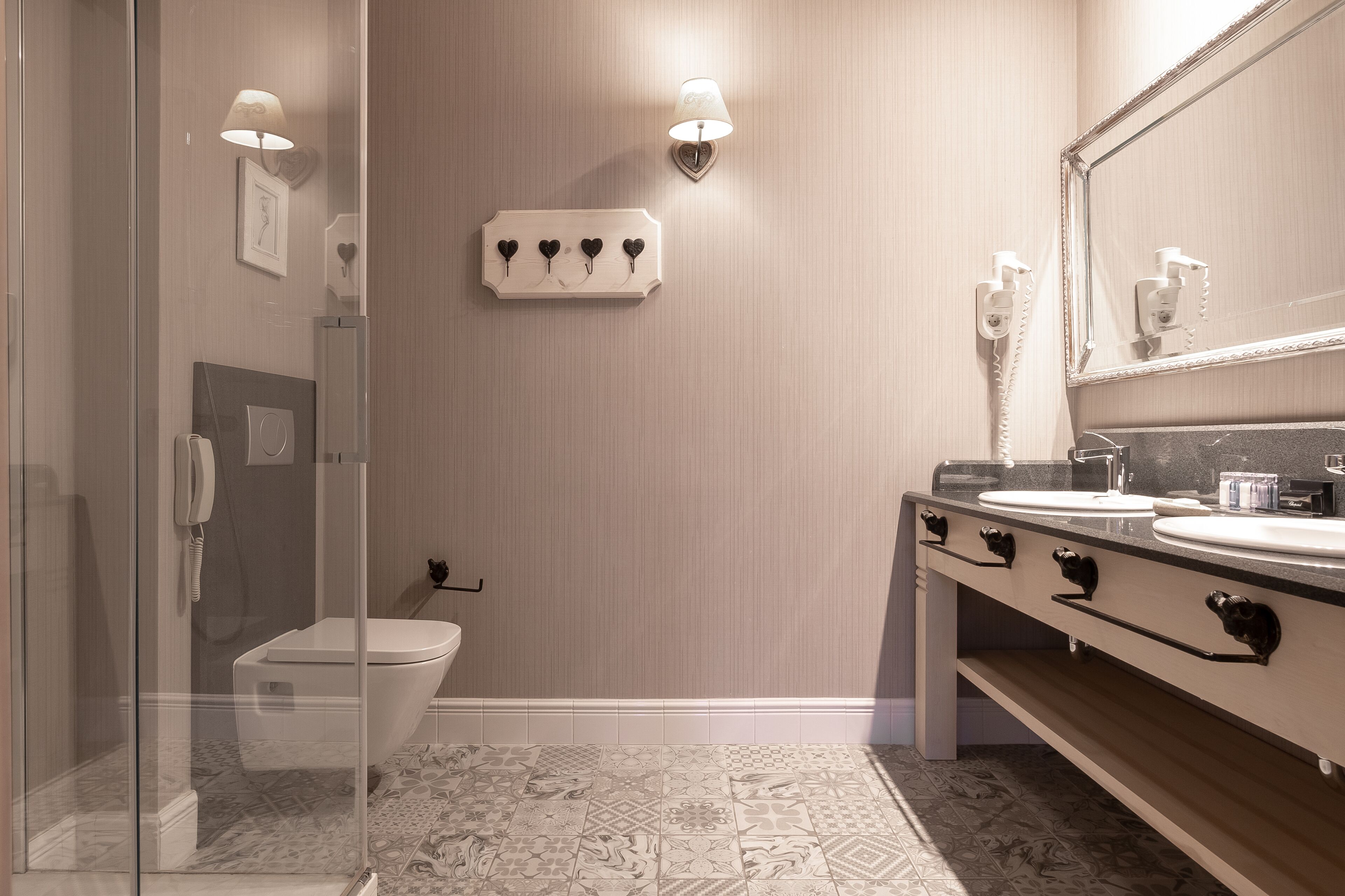 A modern bathroom with a glass shower enclosure, a toilet, a vanity with a large mirror, and a wall-mounted light fixture.