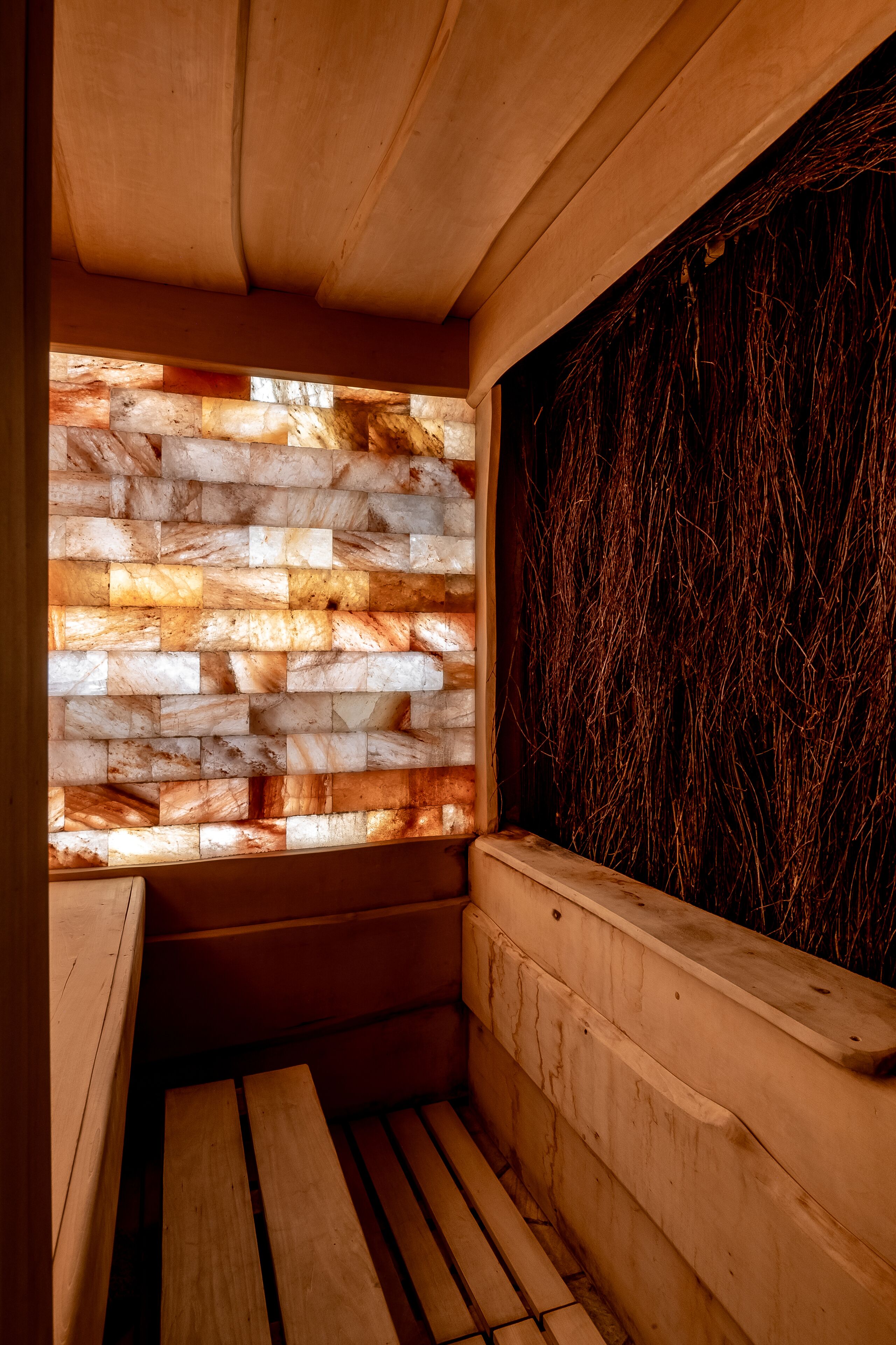 Una sauna con un banco de madera, una pared de piedra con diseño de ladrillo y una pared con superficie oscura y texturizada.