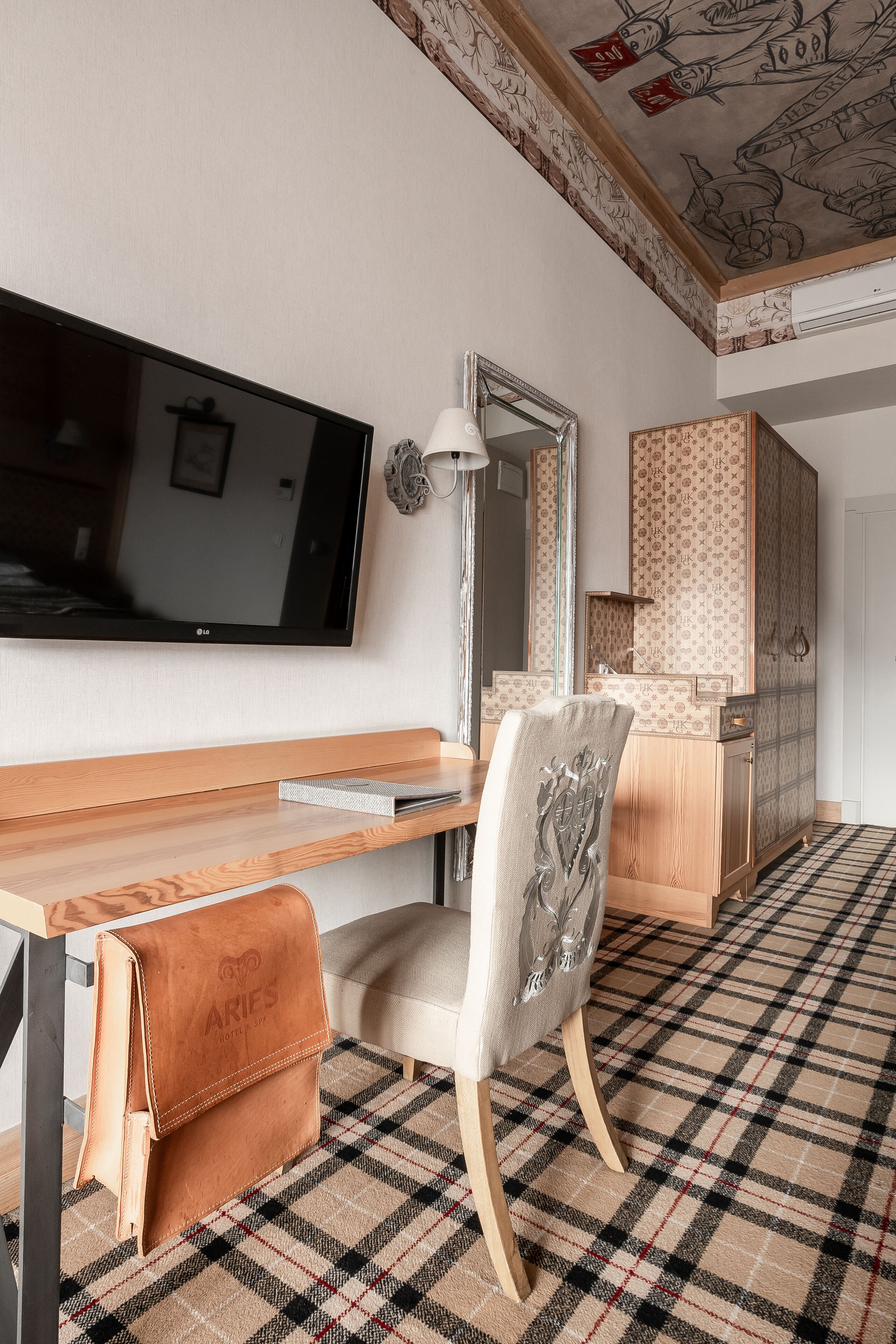 Een moderne hotelkamer met een flatscreen televisie, een houten bureau, een stoel, een spiegel en een kledingkast.