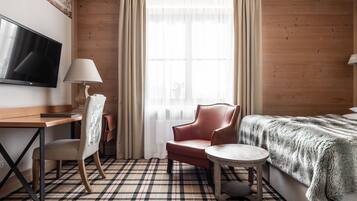 Habitación de hotel con piso de madera, cama con manta de piel, escritorio con televisor, una silla y una lámpara.