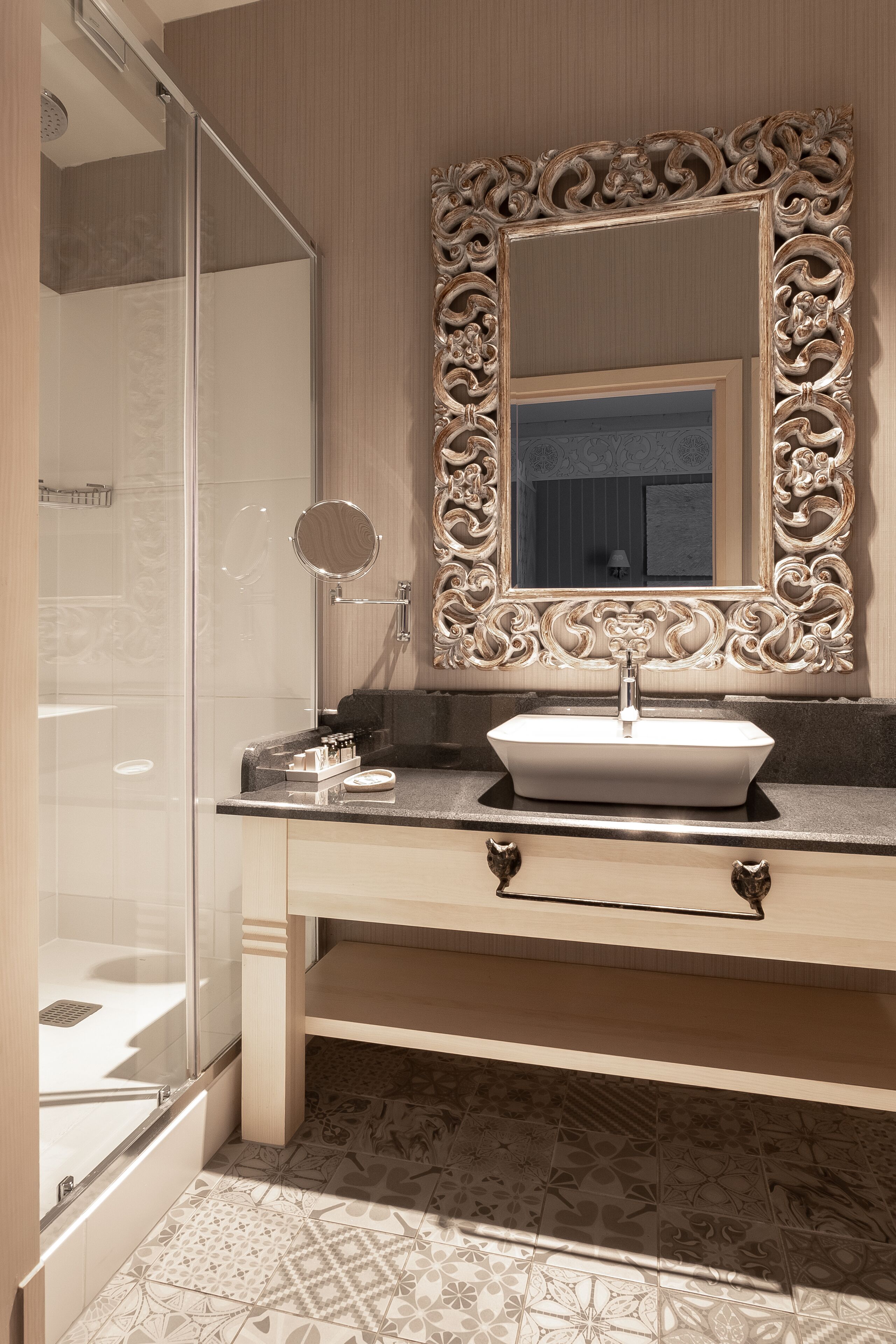 A bathroom with a large ornate mirror, a white sink, and a shower area.