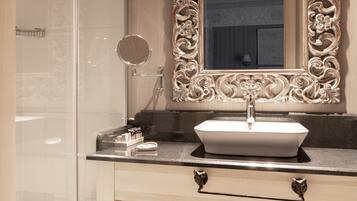 A bathroom with a large ornate mirror, a white sink, and a shower area.