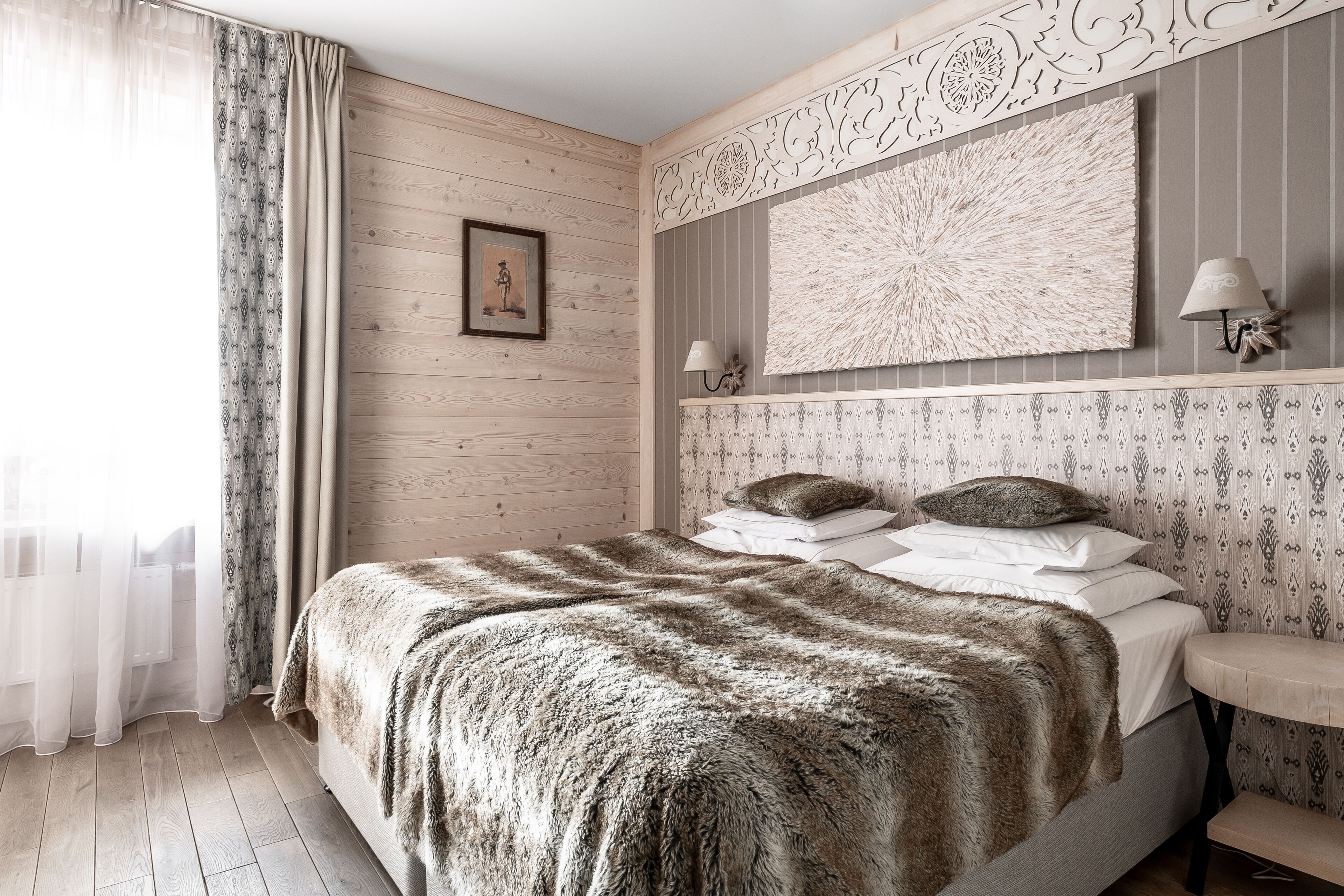 Un dormitorio con cabecera de madera, una cama grande con manta de piel, una mesita de noche con lámpara y un adorno en la pared.