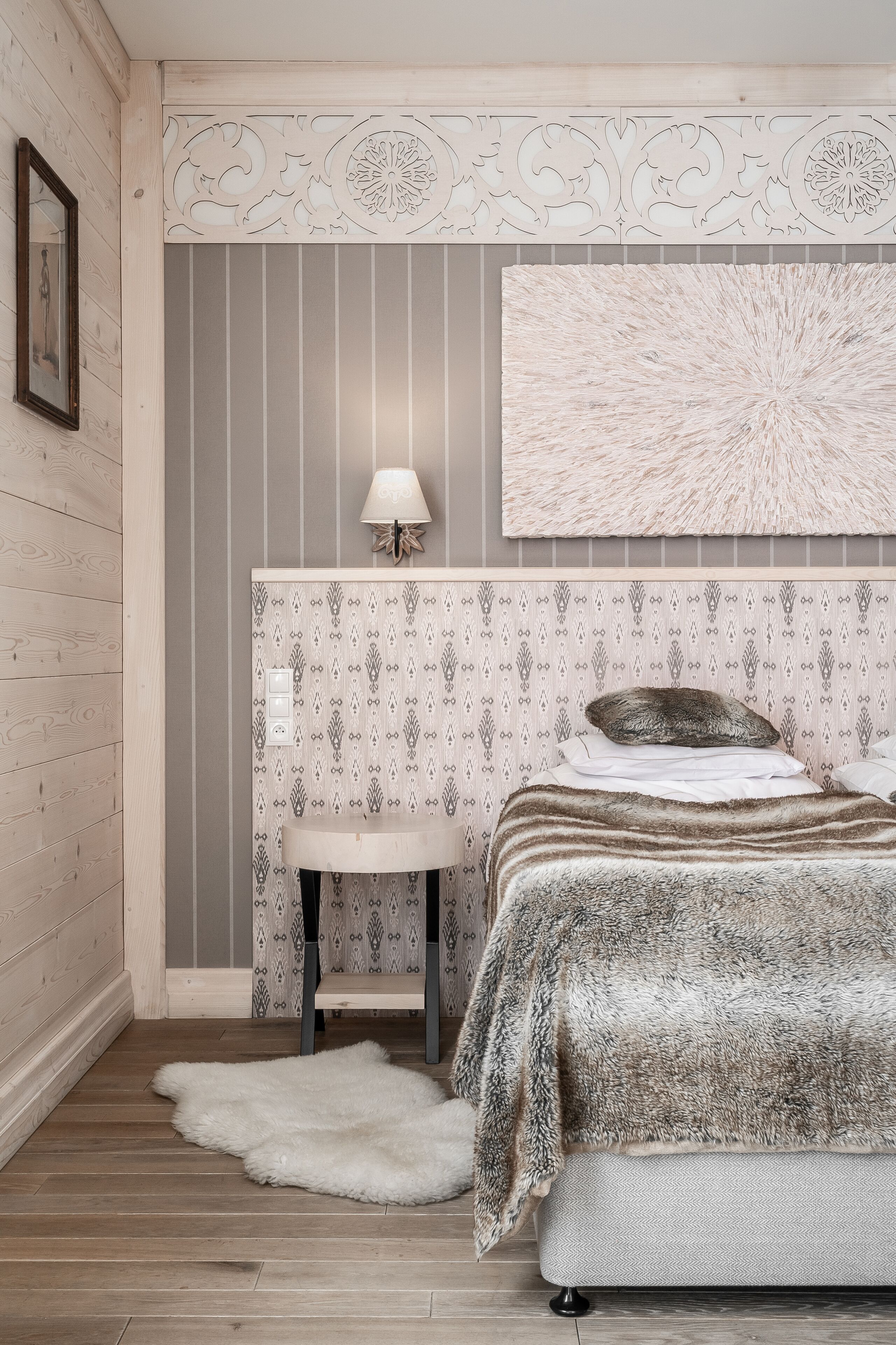 A bedroom with a bed, a bedside table, a lamp, and a decorative wall panel.