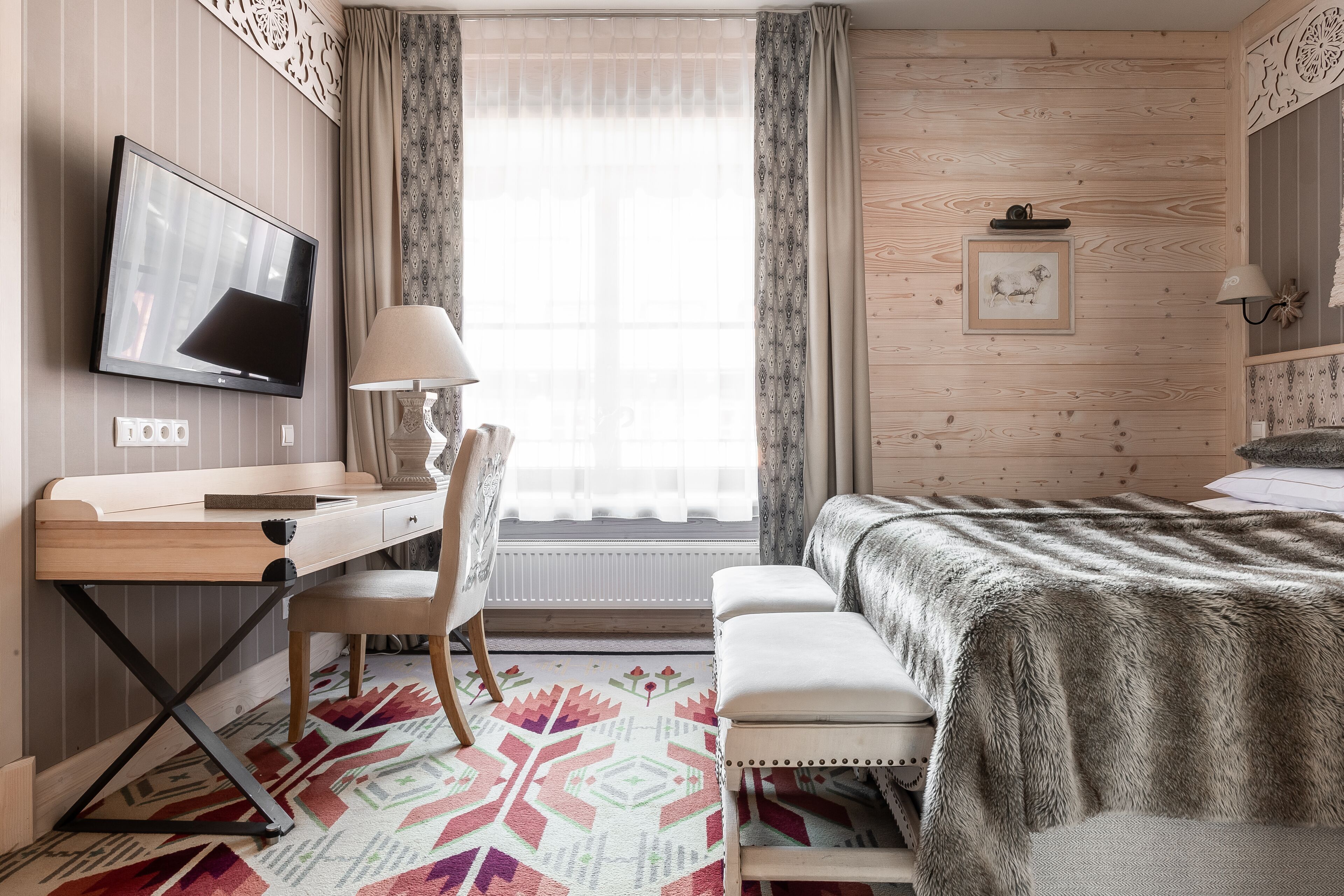 Ein Hotelzimmer mit einem Holztisch, einem Fernseher, einem Bett mit gemustertem Überwurf und einem Fenster mit Vorhängen.