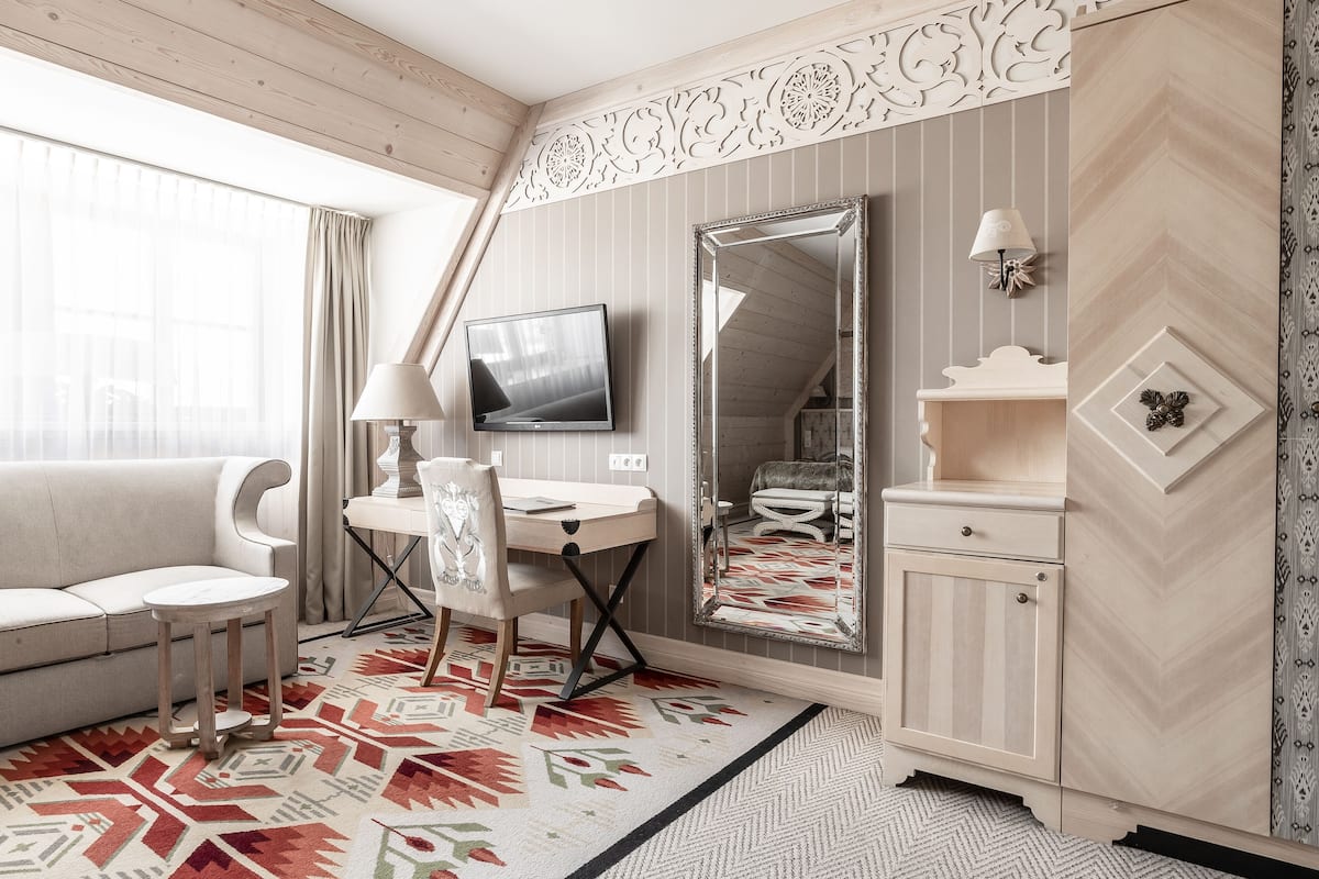 A room with a sofa, a desk, a chair, a television, a mirror, and a cabinet.