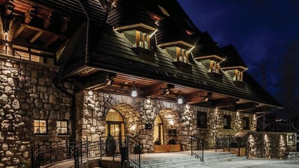 A stone building with a stone facade, wooden beams, and multiple windows with lights. - ARIES Hotel & SPA (Zakopane)