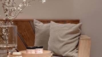 A modern living room with a wooden sofa, a glass vase with branches, and a small table with a candle and a container.
