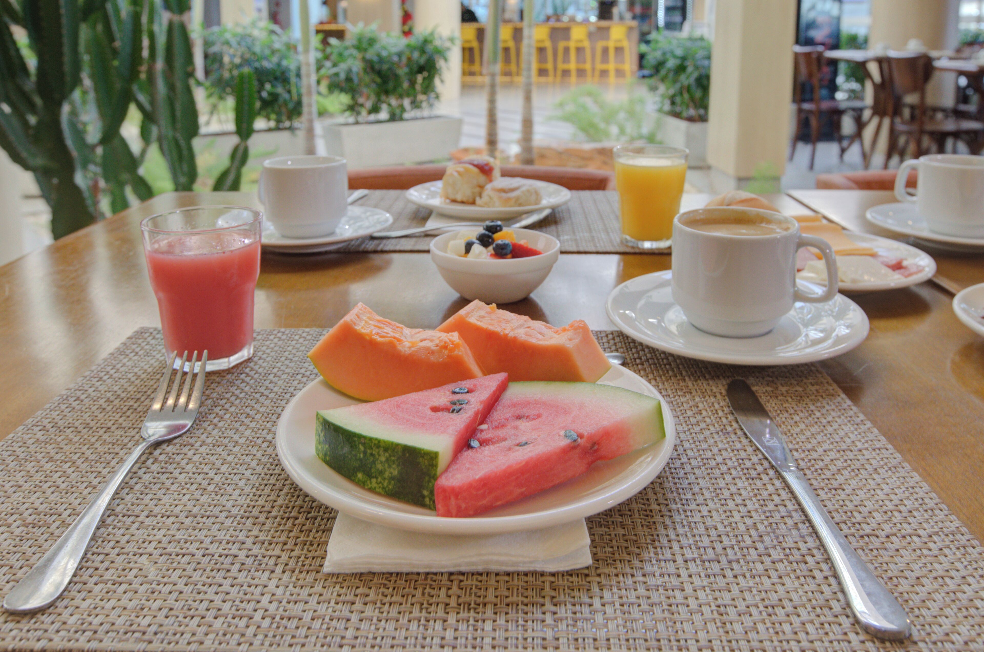 Una mesa de desayuno con una rebanada de sandía, un vaso de jugo de naranja y una taza de café.