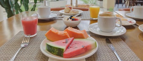 Una mesa de desayuno con una rebanada de sandía, un vaso de jugo de naranja y una taza de café.