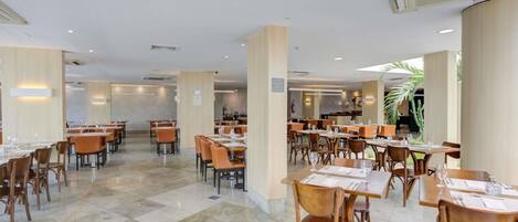 Un comedor interior amplio con varias mesas y sillas, suelo de baldosas y vistas al exterior.