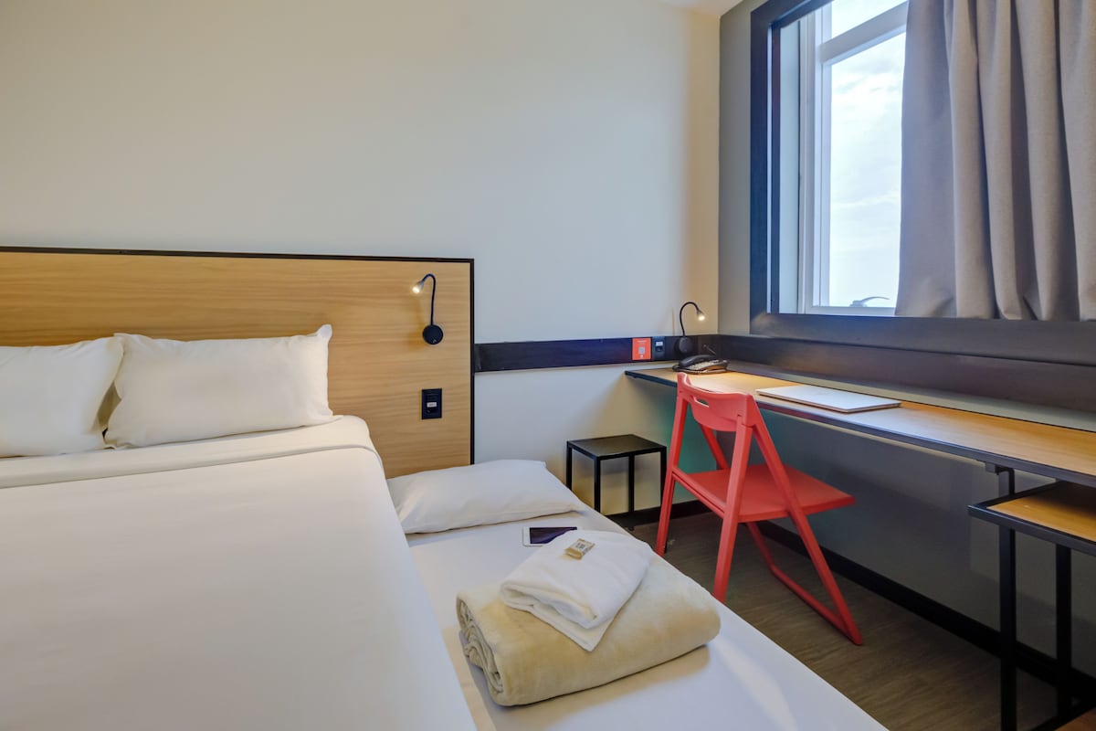 A hotel room with a bed, a desk, a chair, and a window.