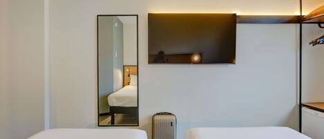 A hotel room with two beds, a mirror, a wall-mounted shelf, a suitcase, and a wardrobe.