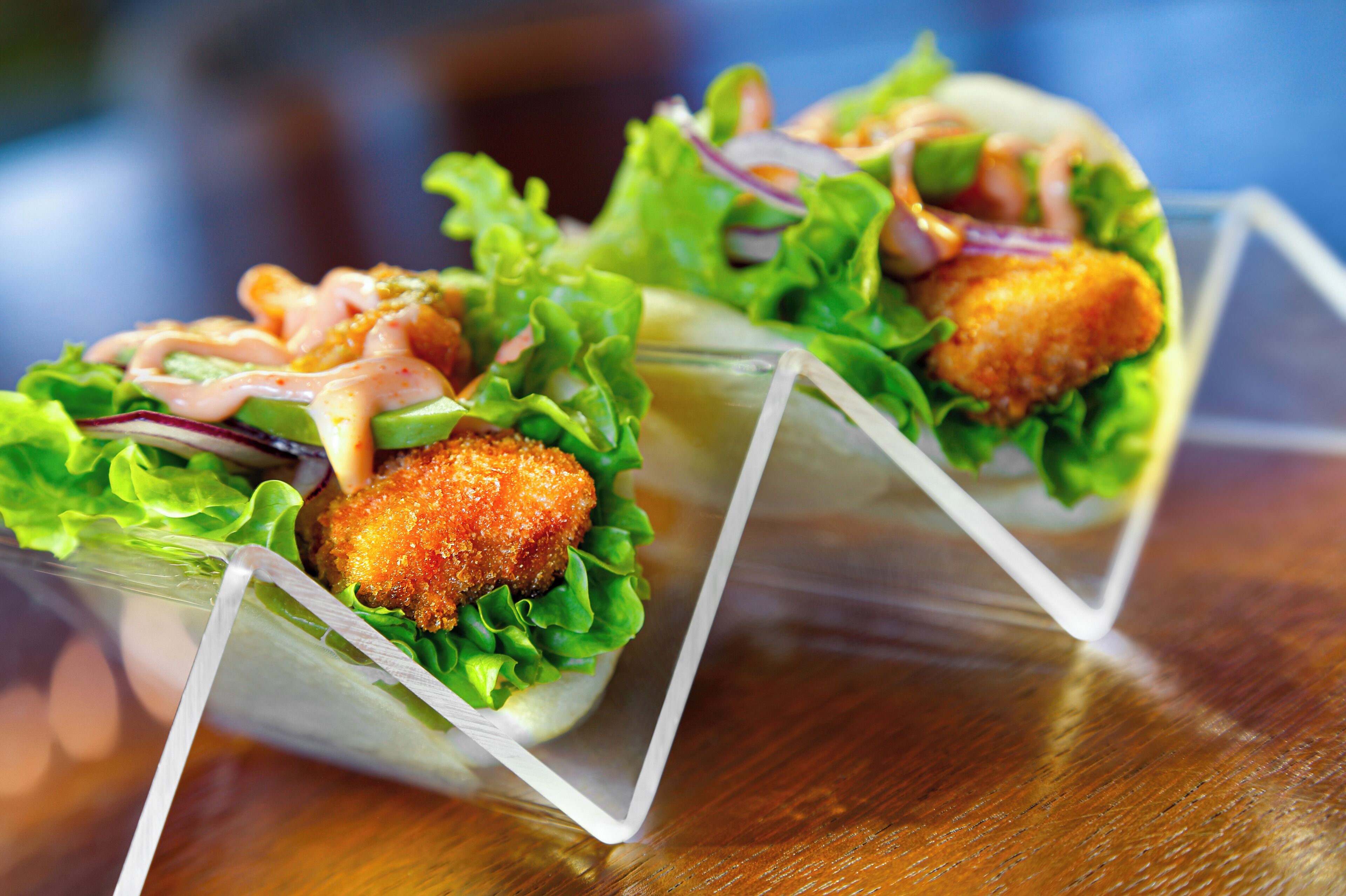 Two food items in clear containers with lettuce and a sauce.