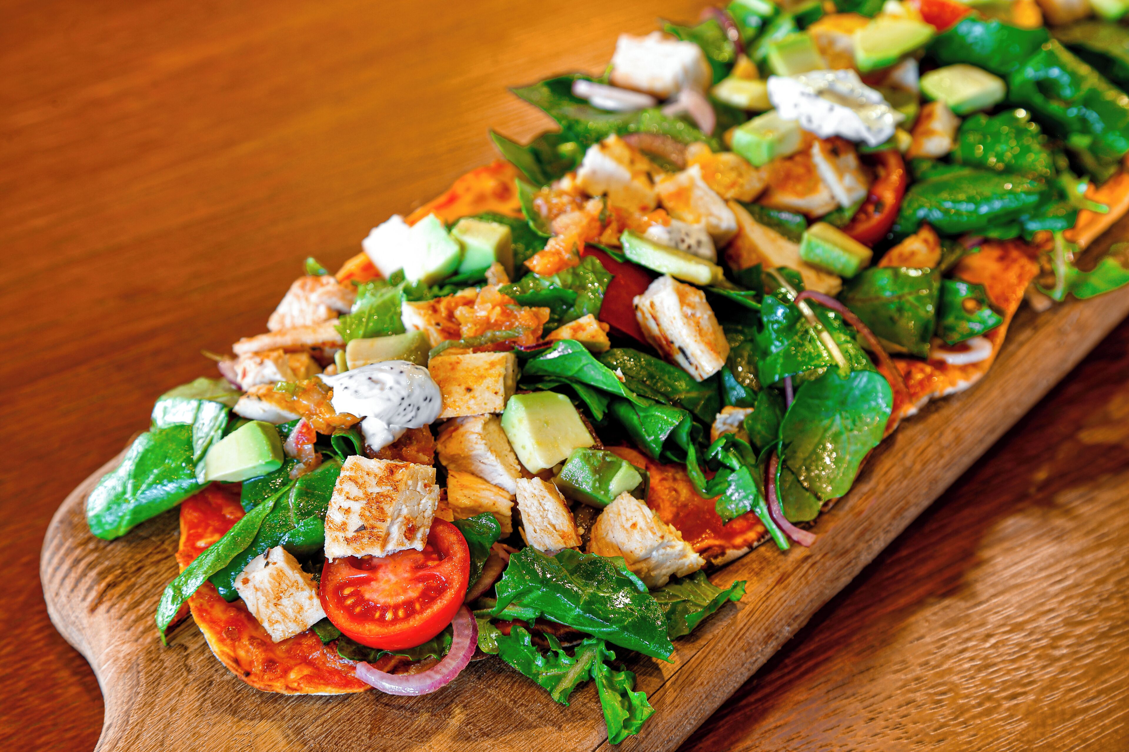 Uma tábua de madeira com uma salada contendo diversos vegetais e pedaços de frango.