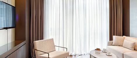 Et moderne hotelværelse med sofa, stol, sofabord og tv.