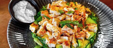 Un plato de comida con pollo, aguacate y verduras, además de un recipiente pequeño con salsa.