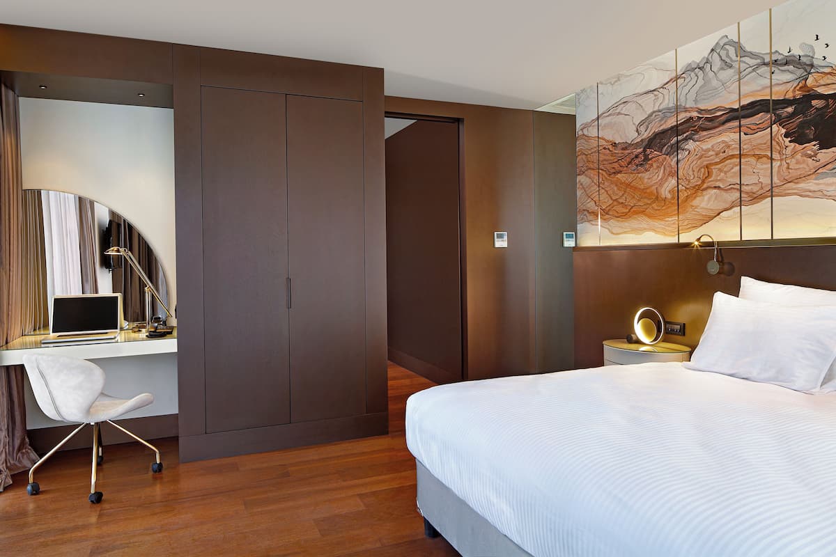 Una habitación de hotel moderna con cama, escritorio, silla y un cuadro abstracto grande en la pared.