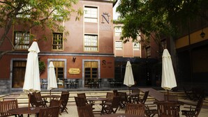 An outdoor patio with wooden tables and chairs, umbrellas, and a building with a sign reading "La Cuina Nativa."