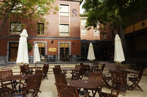 Un patio al aire libre con mesas y sillas de madera, sombrillas y un edificio con un letrero que dice "La Cuina Nativa".