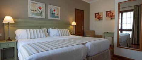 A double bed with a striped bedspread, two bedside lamps, a nightstand, a chair, a desk, and a mirror.
