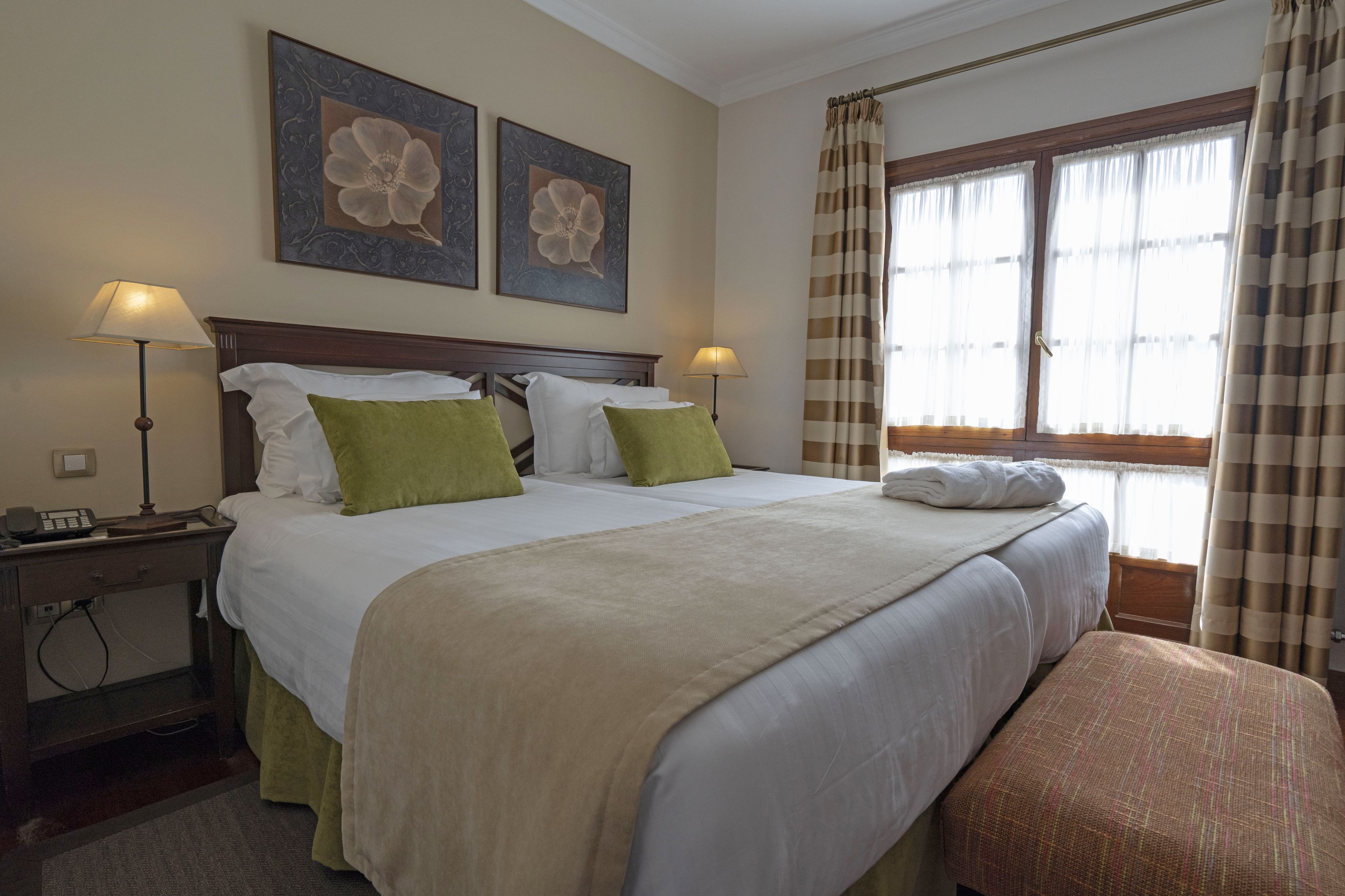 Habitación de hotel con una cama grande, dos lámparas de noche, un escritorio con teléfono y dos cuadros florales.