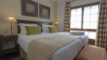 Habitación de hotel con una cama grande, dos lámparas de noche, un escritorio con teléfono y dos cuadros florales.