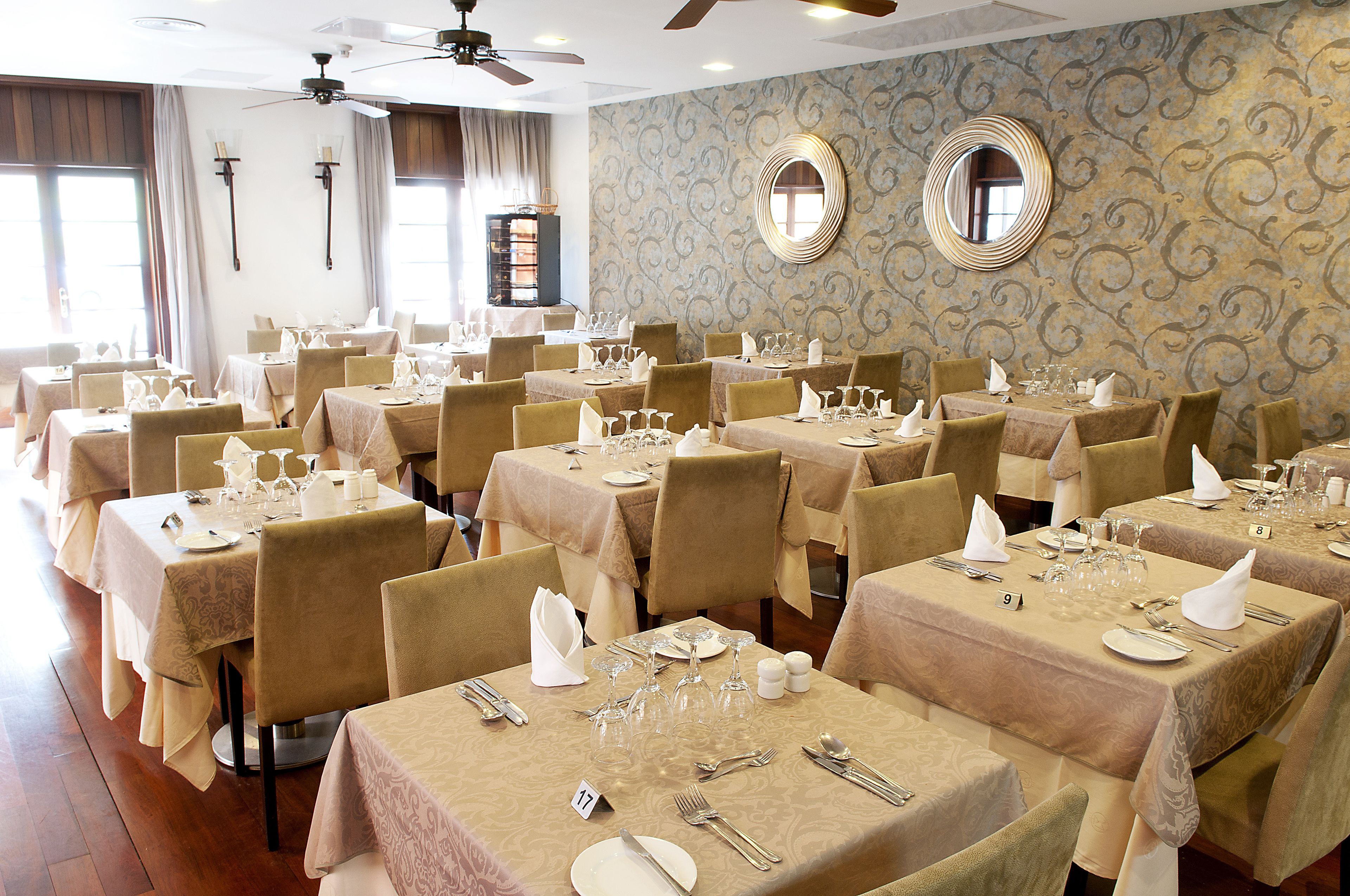 Une vaste salle de banquet, avec de nombreuses tables dressées pour le repas, chacune étant agrémentée de chaises et de couverts.