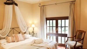 A bedroom with a large bed, a wooden chair, a window with curtains, and a bedside table with a lamp.