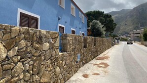 A two-story building with a stone wall and blue exterior. - B&B Pelagos (Castellammare del Golfo)