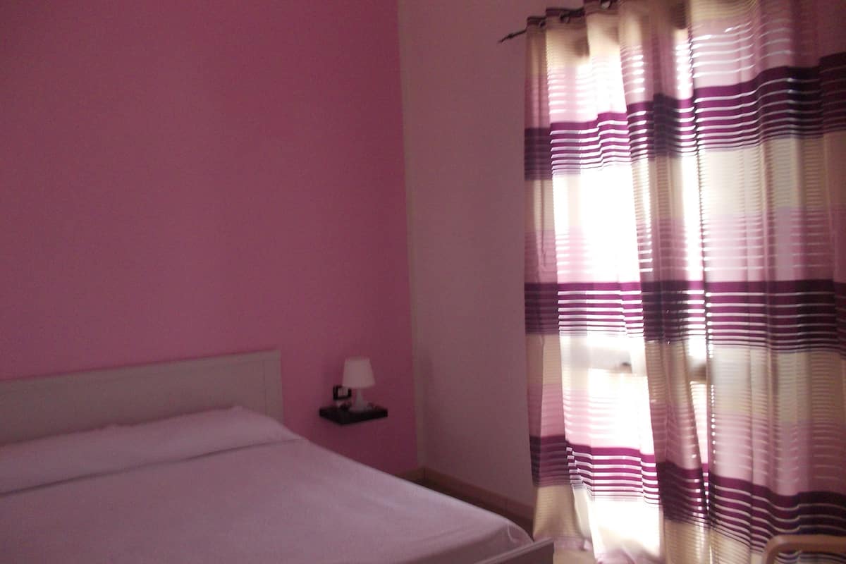 Ein Schlafzimmer mit einem Einzelbett, einem Nachttisch mit Lampe und einem Fenster mit gestreifteren Vorhängen.