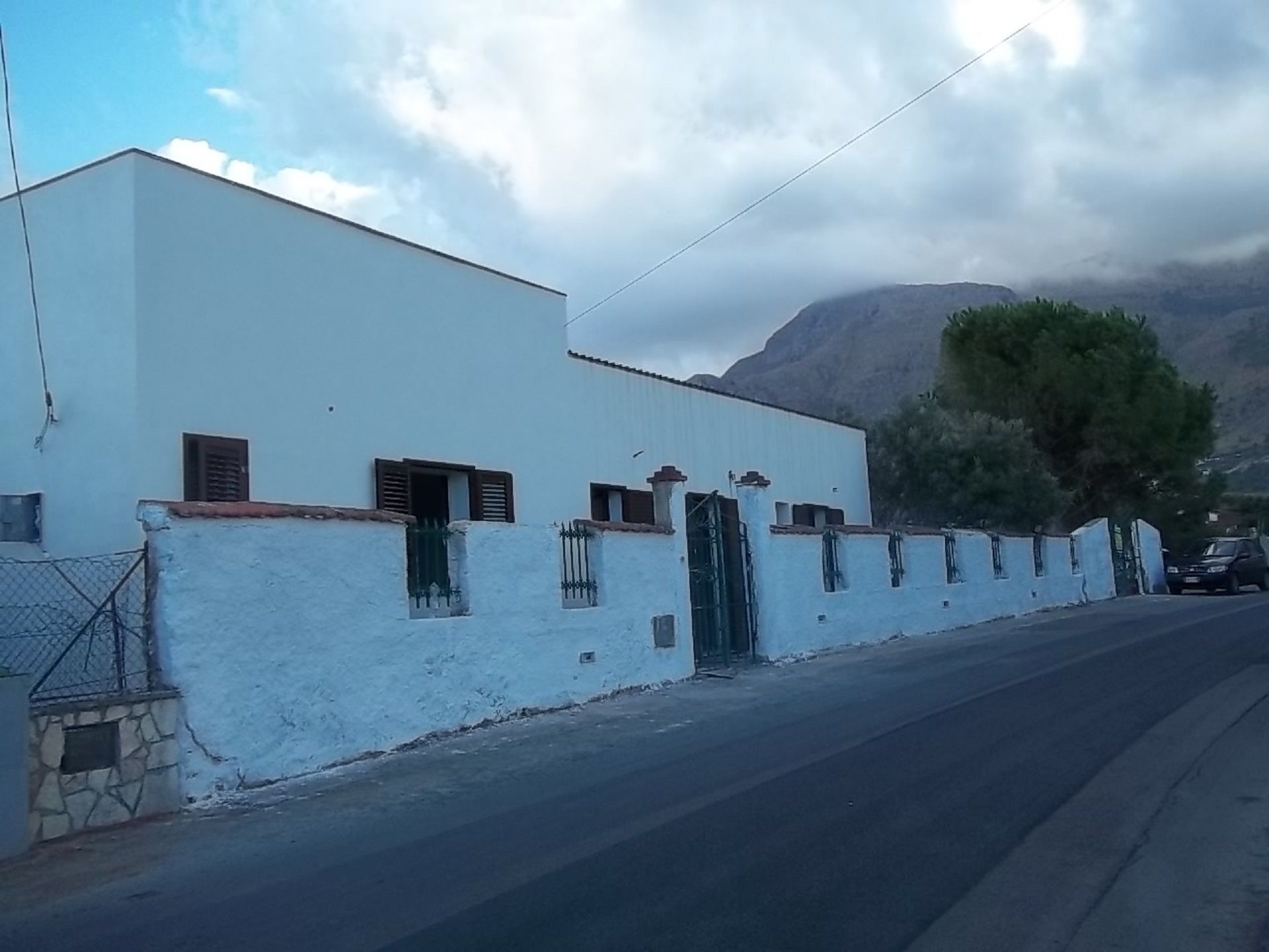A white building with a stone base, a metal fence, and a mountain in the background.