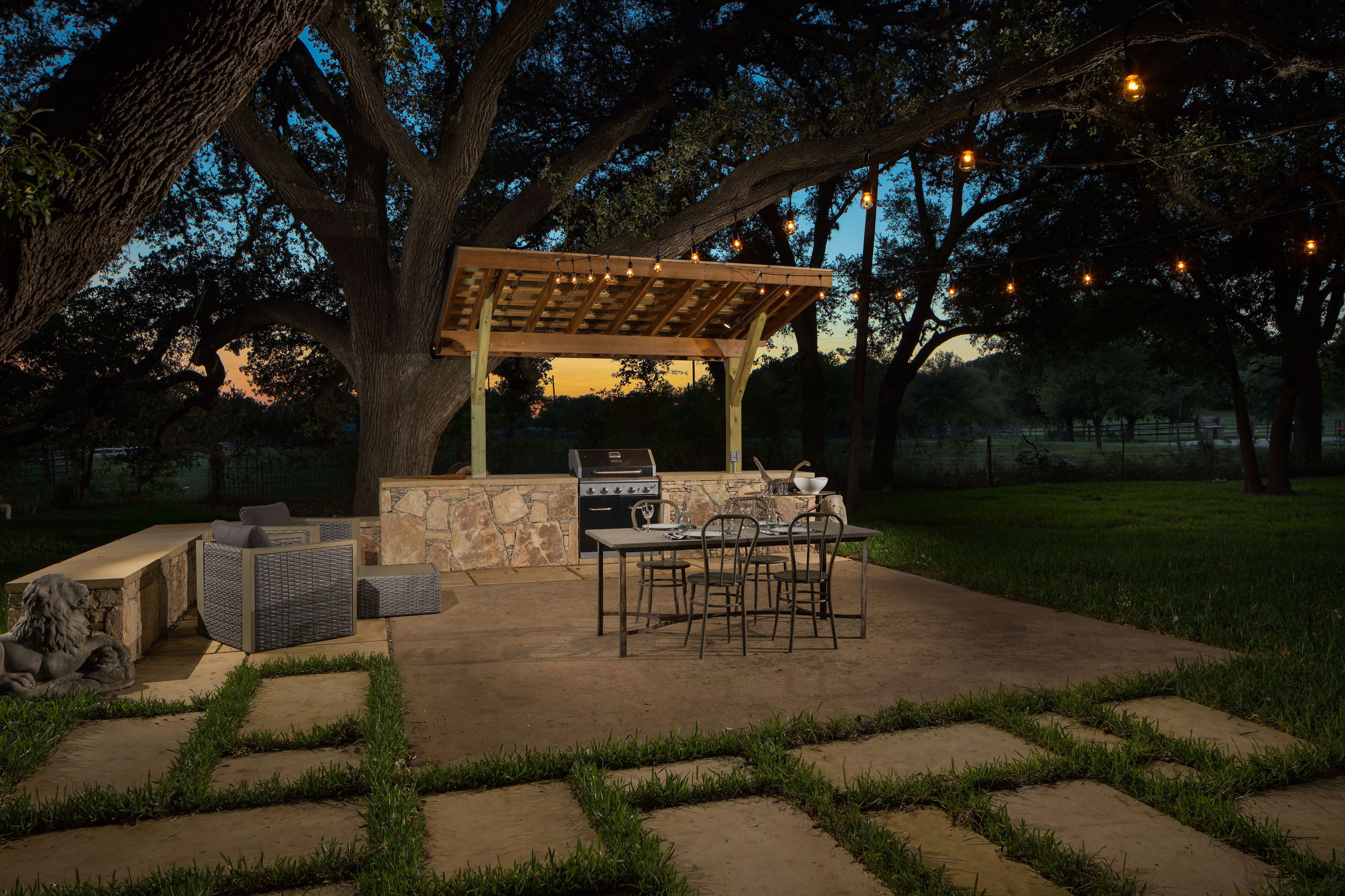 An outdoor patio with a pergola, stone barbecue, and seating area.
