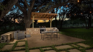 An outdoor patio with a pergola, stone barbecue, and seating area.