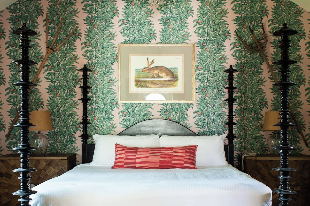 Ein Schlafzimmer mit Himmelbett, einer Chandelieber und einer gerahmten botanischen Illustration an der Wand.
