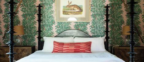 A bedroom with a four-poster bed, a chandelier, and a framed botanical illustration on the wall.
