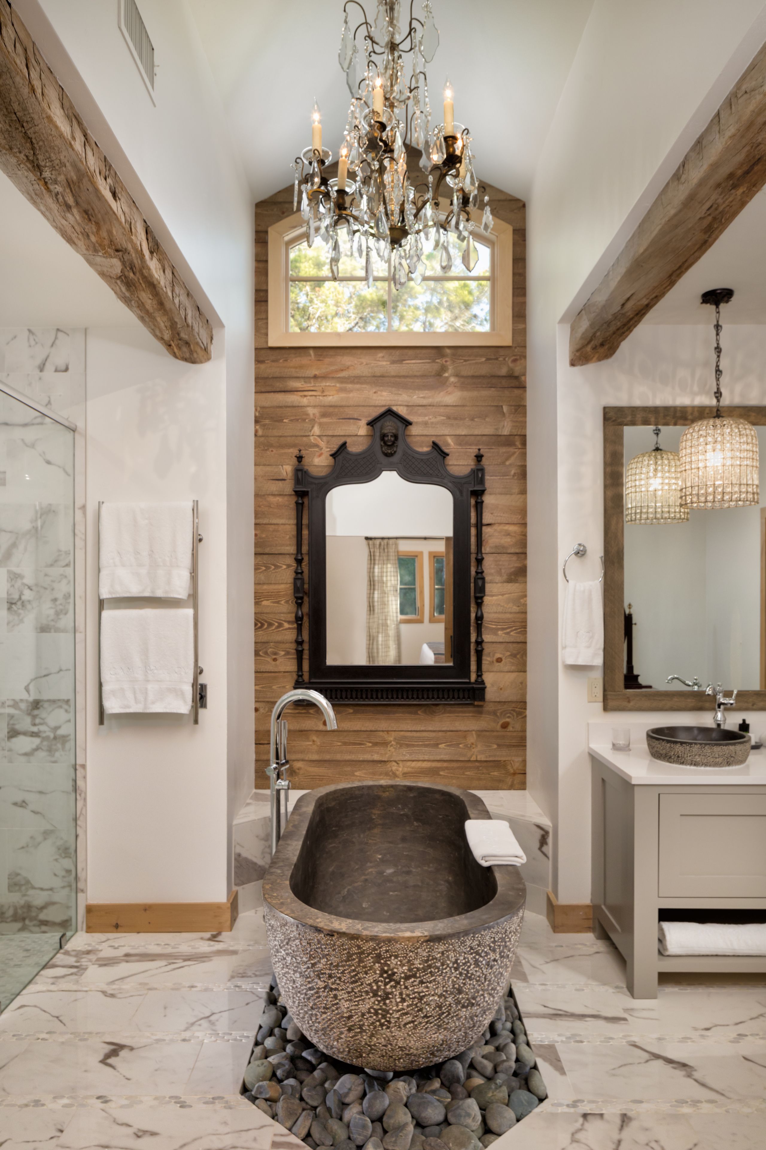 A bathroom with a freestanding bathtub, a large mirror, and a chandelier.