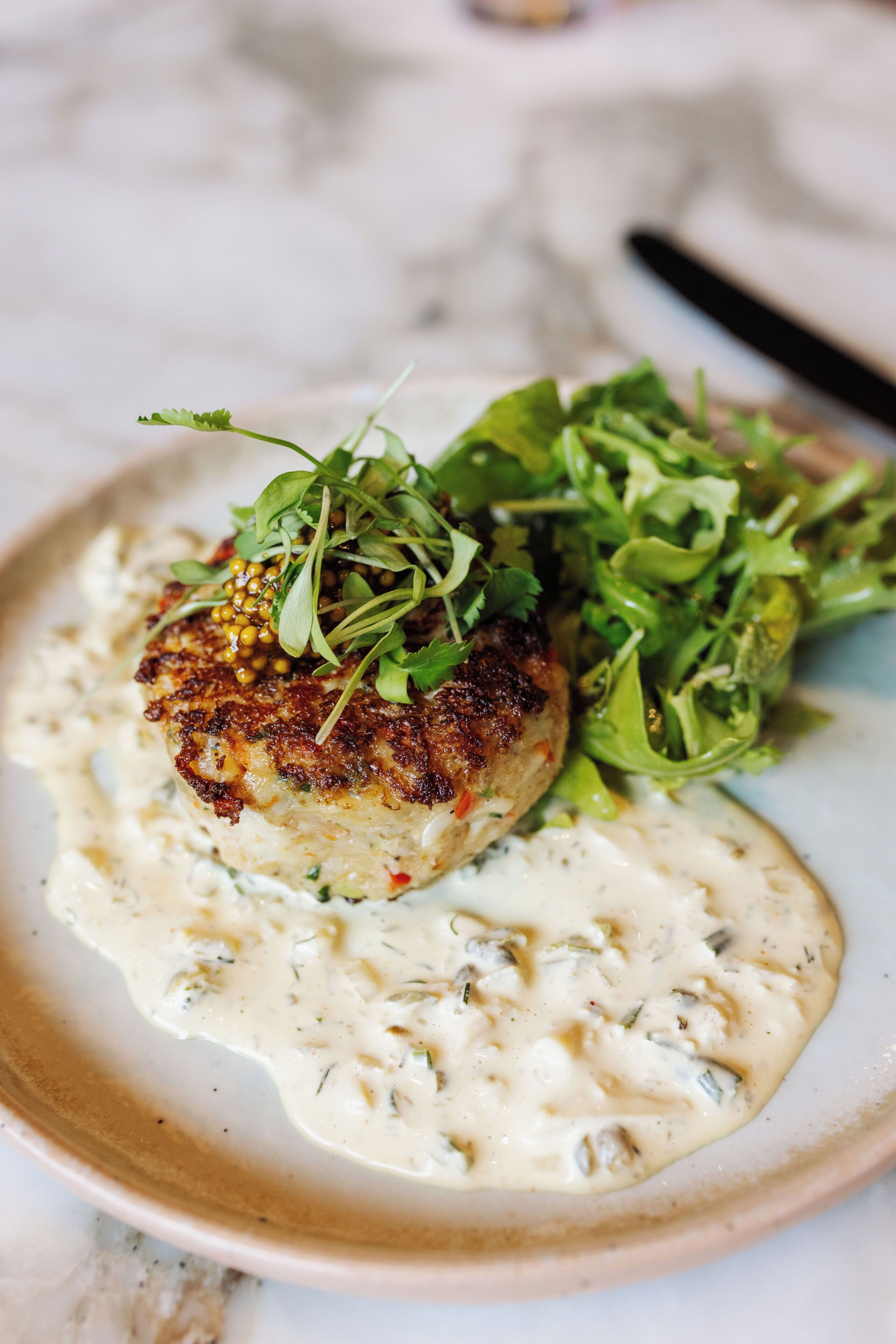 A plate with a seared scallop, a creamy sauce, and a side of greens.