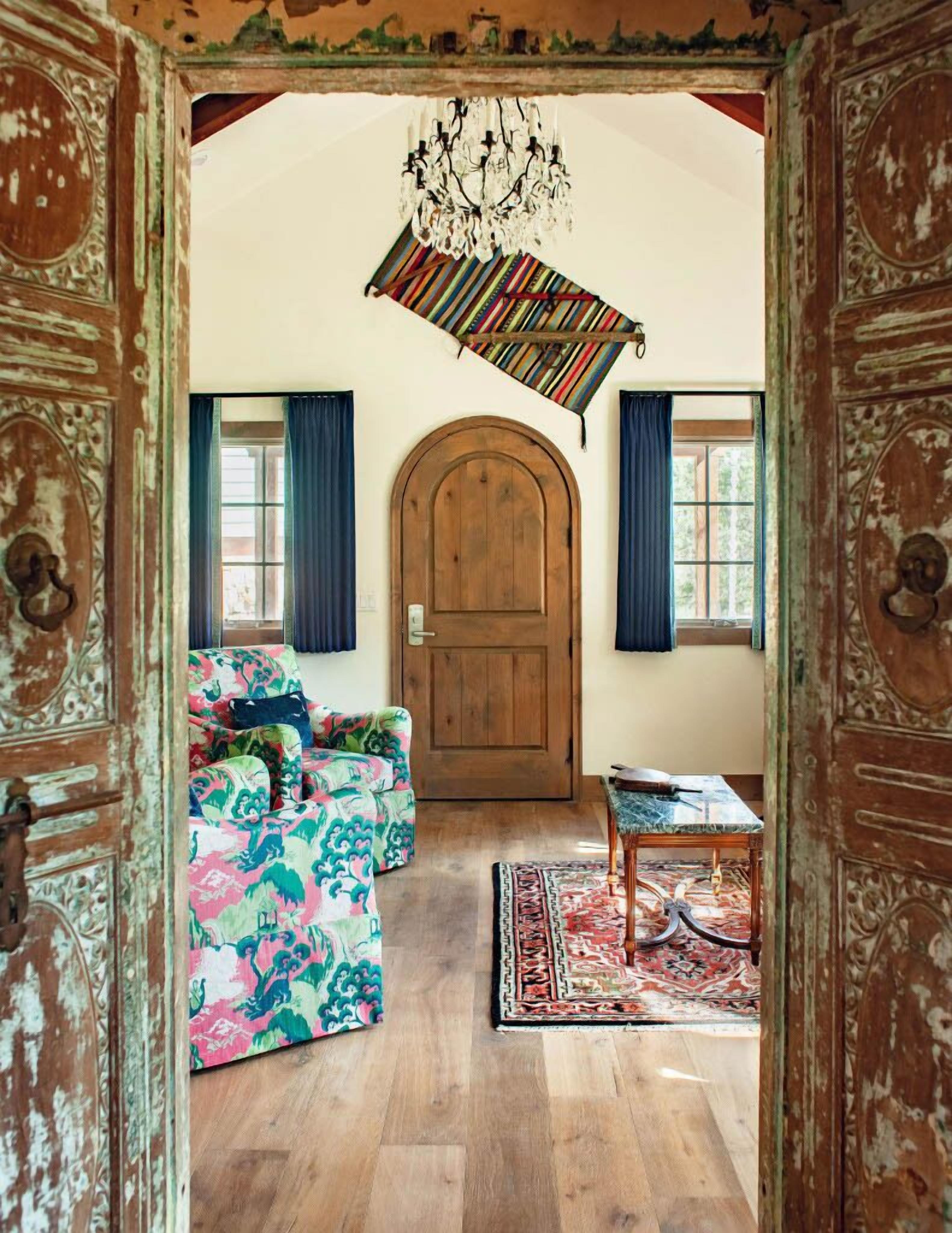 Una stanza con una porta in legno, un divano colorato, un tavolino e un tappeto decorato.