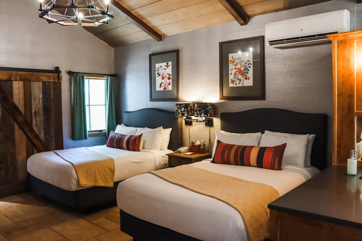 Ein Hotelzimmer mit zwei Betten, einer Holzbalkendecke, einem Chandelier, gerahmten Kunstwerken und einer Klimaanlage.