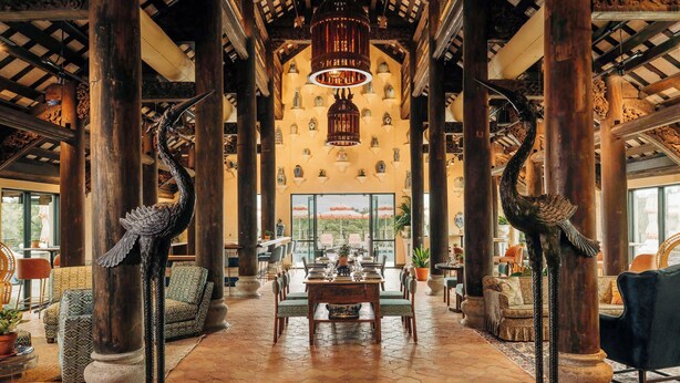 A spacious lobby with high wooden columns, a central dining table, and decorative bird sculptures. - Camp Lucy (Dripping Springs)
