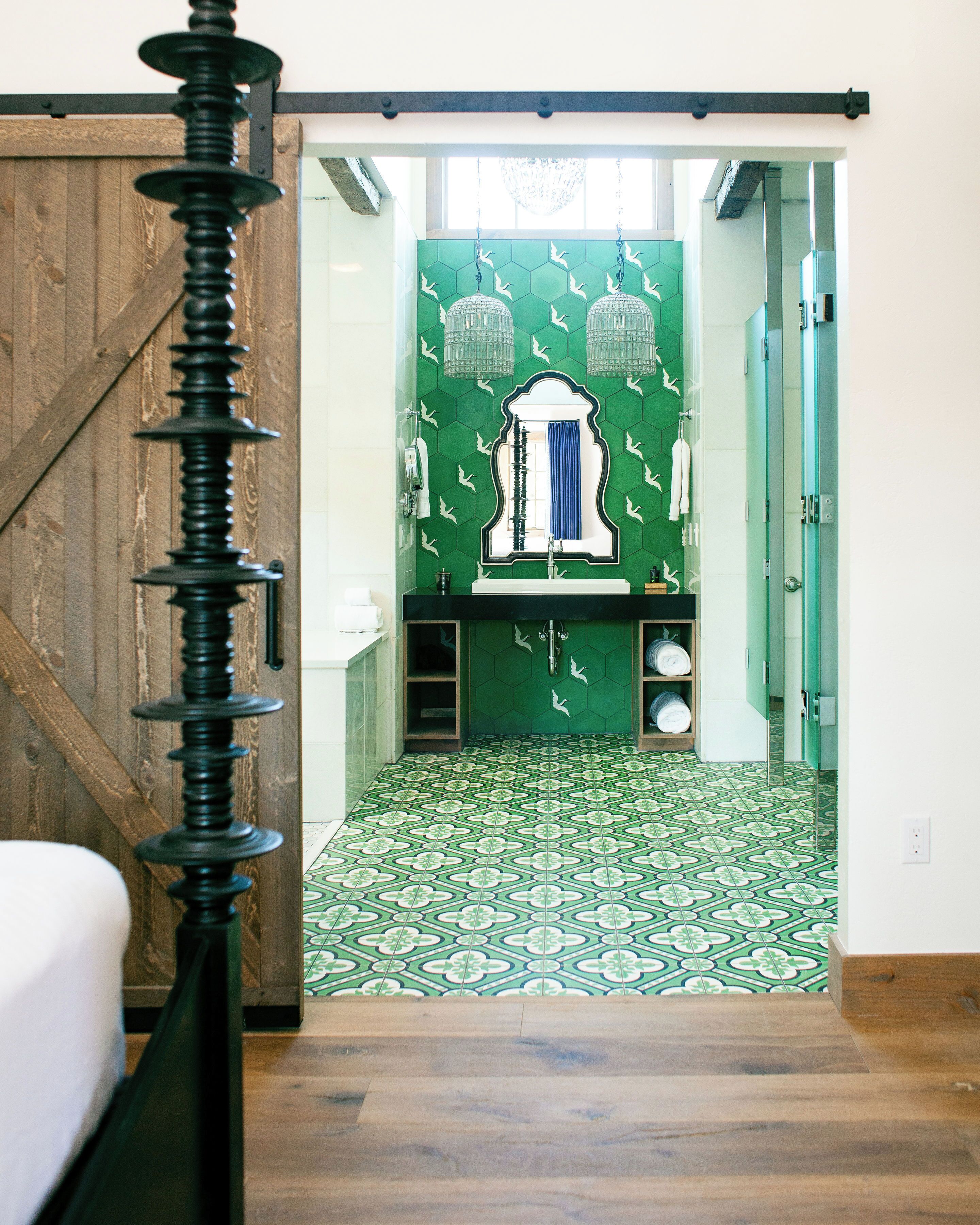 Un baño con pared de azulejos verdes, un lavamanos blanco y un espejo.
