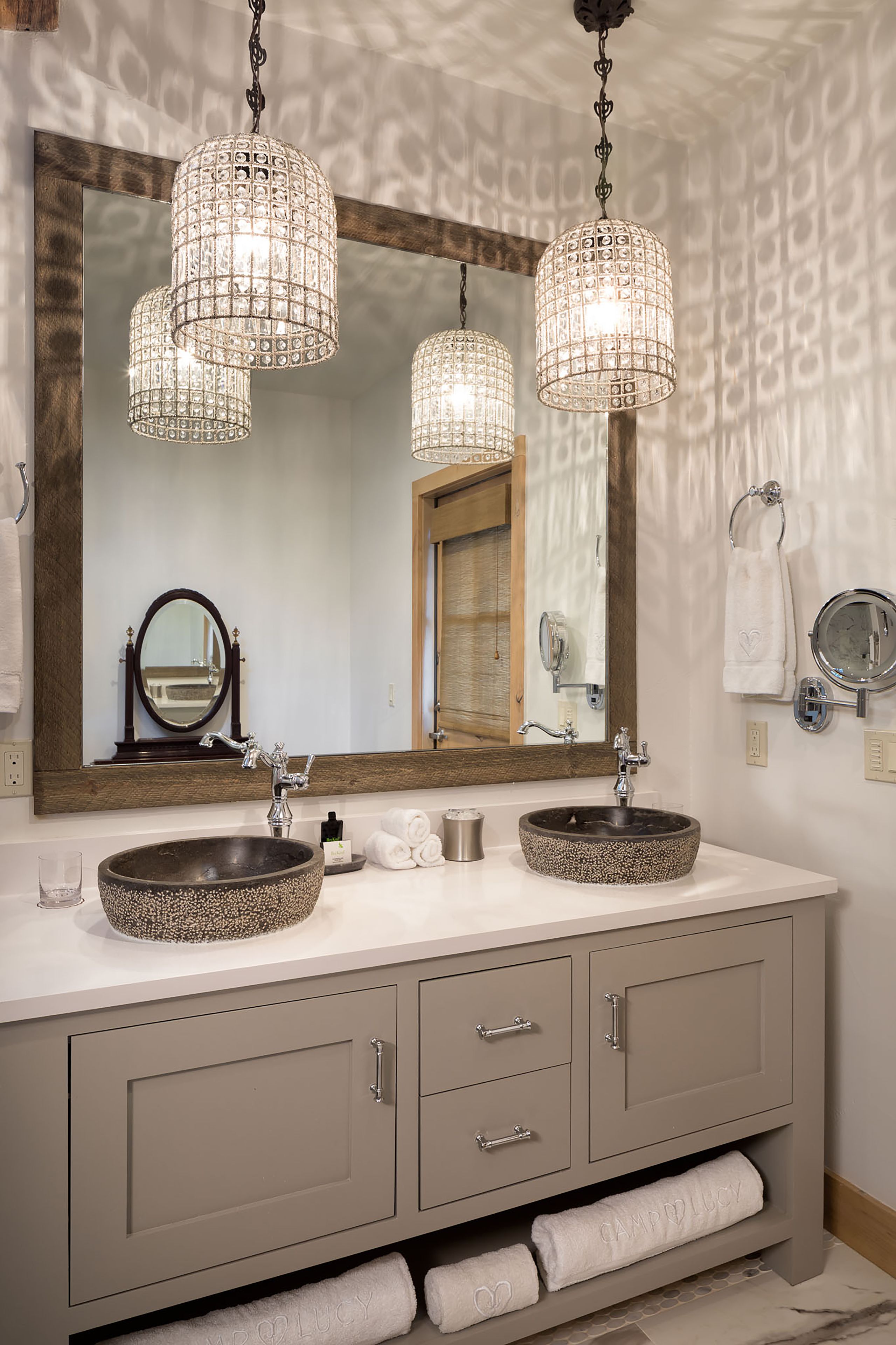 A bathroom with two sinks, a large mirror, and hanging crystal chandeliers.