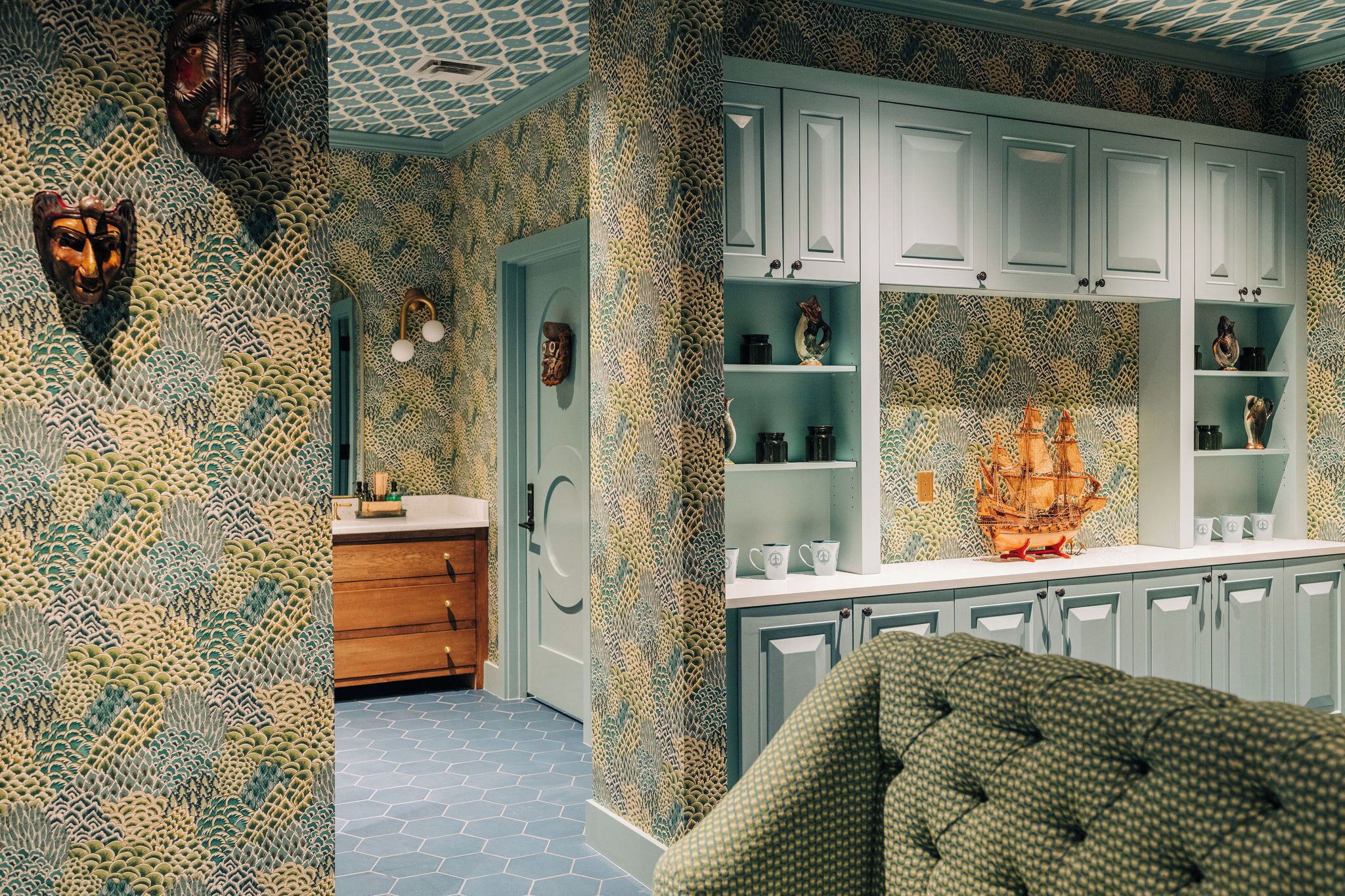 A kitchen with patterned wallpaper, wooden cabinets, and a decorative ship model.